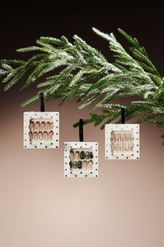 3 chic holiday press-on nail designs hanging from an evergreen