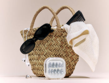 A wicker basket that holds sunglasses, a comb, and a towel. The Sea Salt nails sit in front of the basket.
